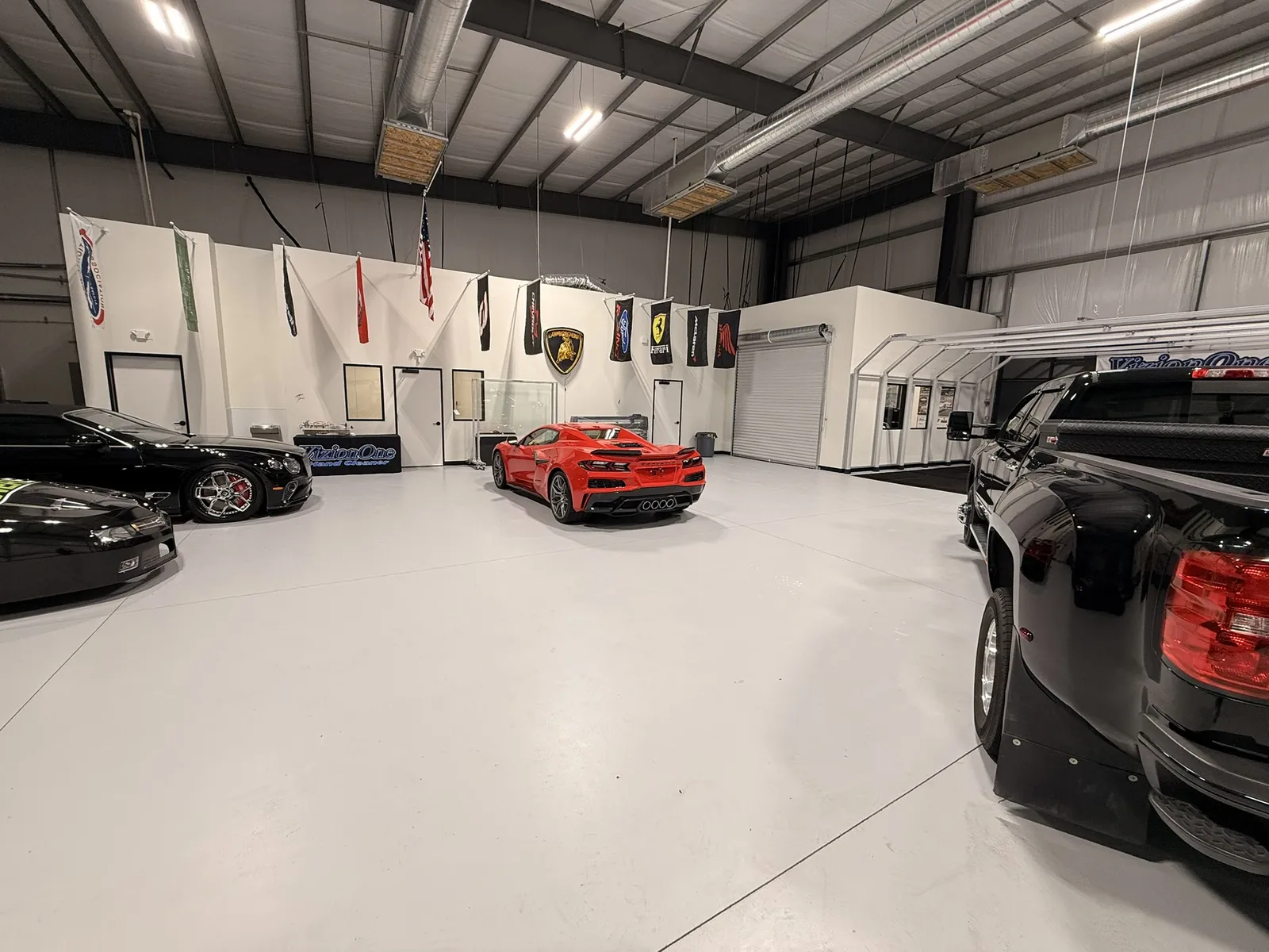 Wide view of the bays with a red Corvette, black cars and flags on the wall