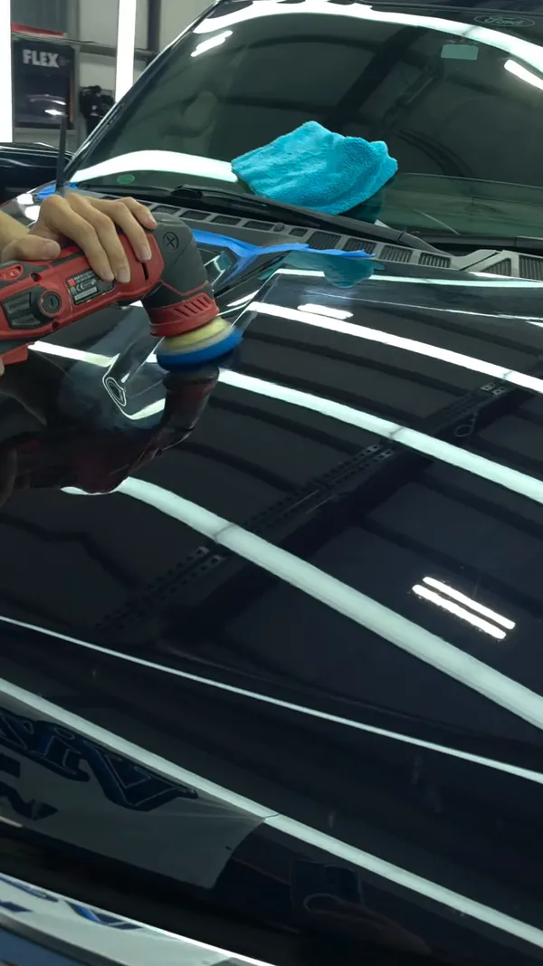 Polishing the hood of a blue Ford F-150 under the light tunnel
