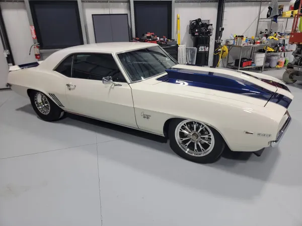 White first-gen Camaro with blue stripes in the shop