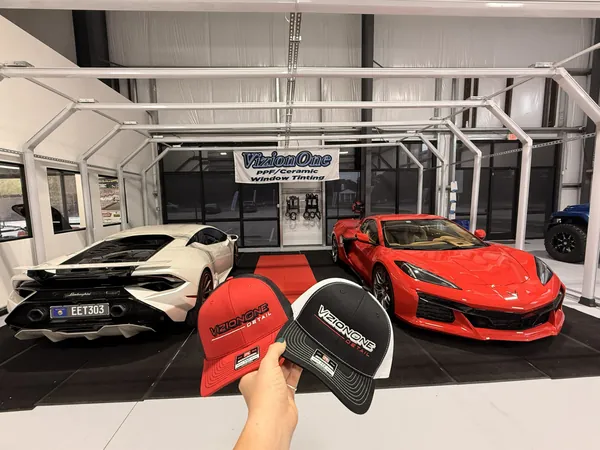 Red and black VizionOne caps, with a Huracán and a Corvette in the bay